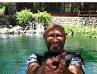 a man is posing for a picture in front of a pond